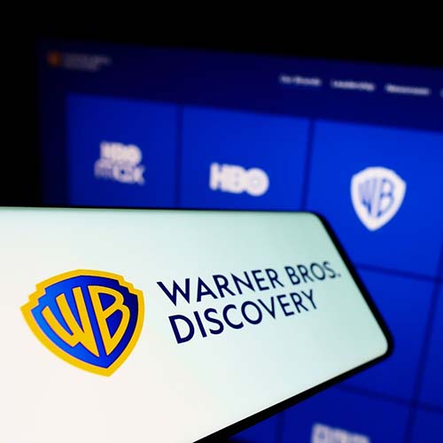 Mobile phone with logo of media company Warner Bros. Discovery Inc. (WBD) on screen in front of business website. Focus on left of phone display.