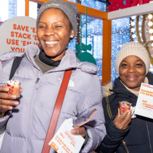 Two women at the Dunkin' Rewards Lounge smiling and eating Dunkin products