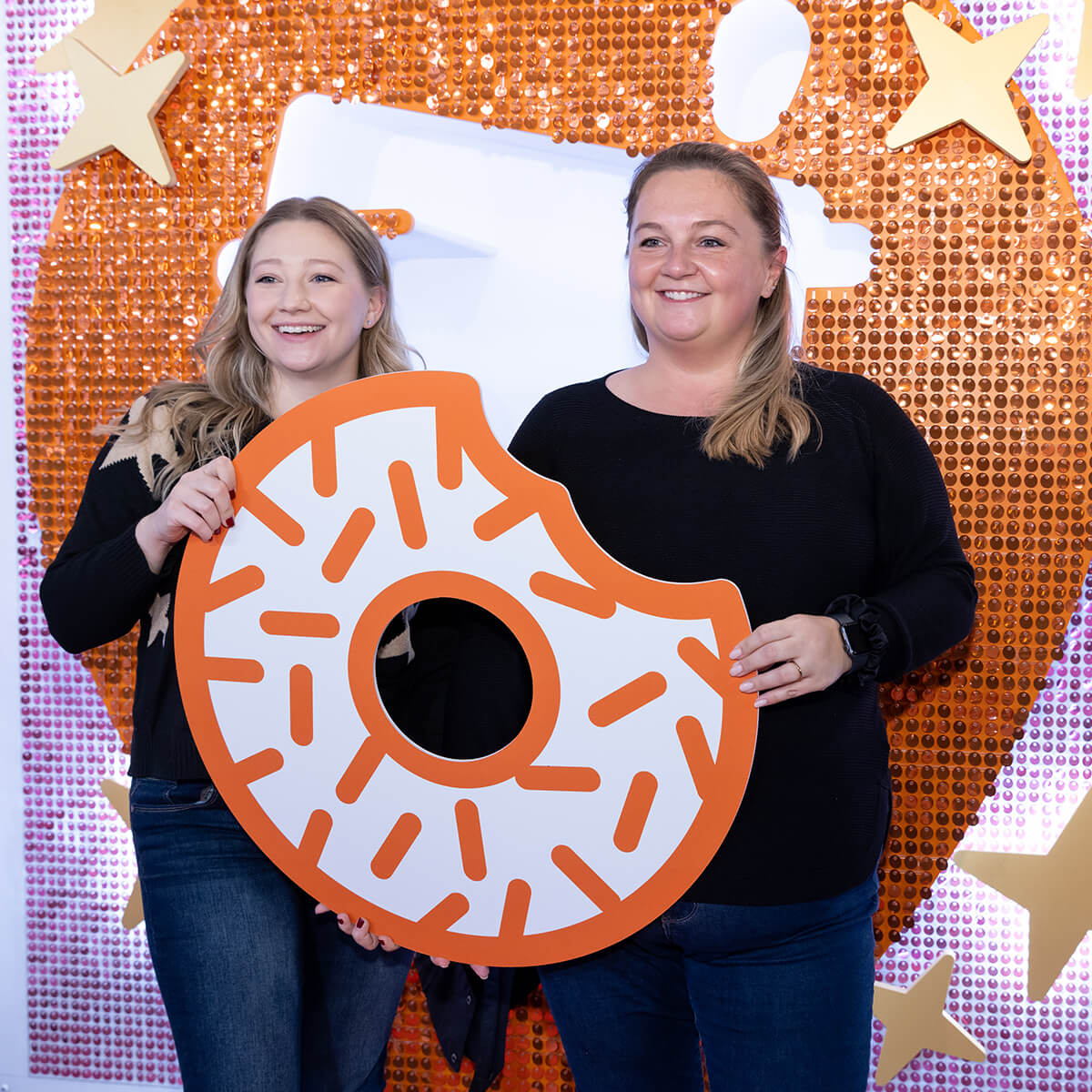 Two women at the Dunkin' Rewards Lounge posing with a donut cut out