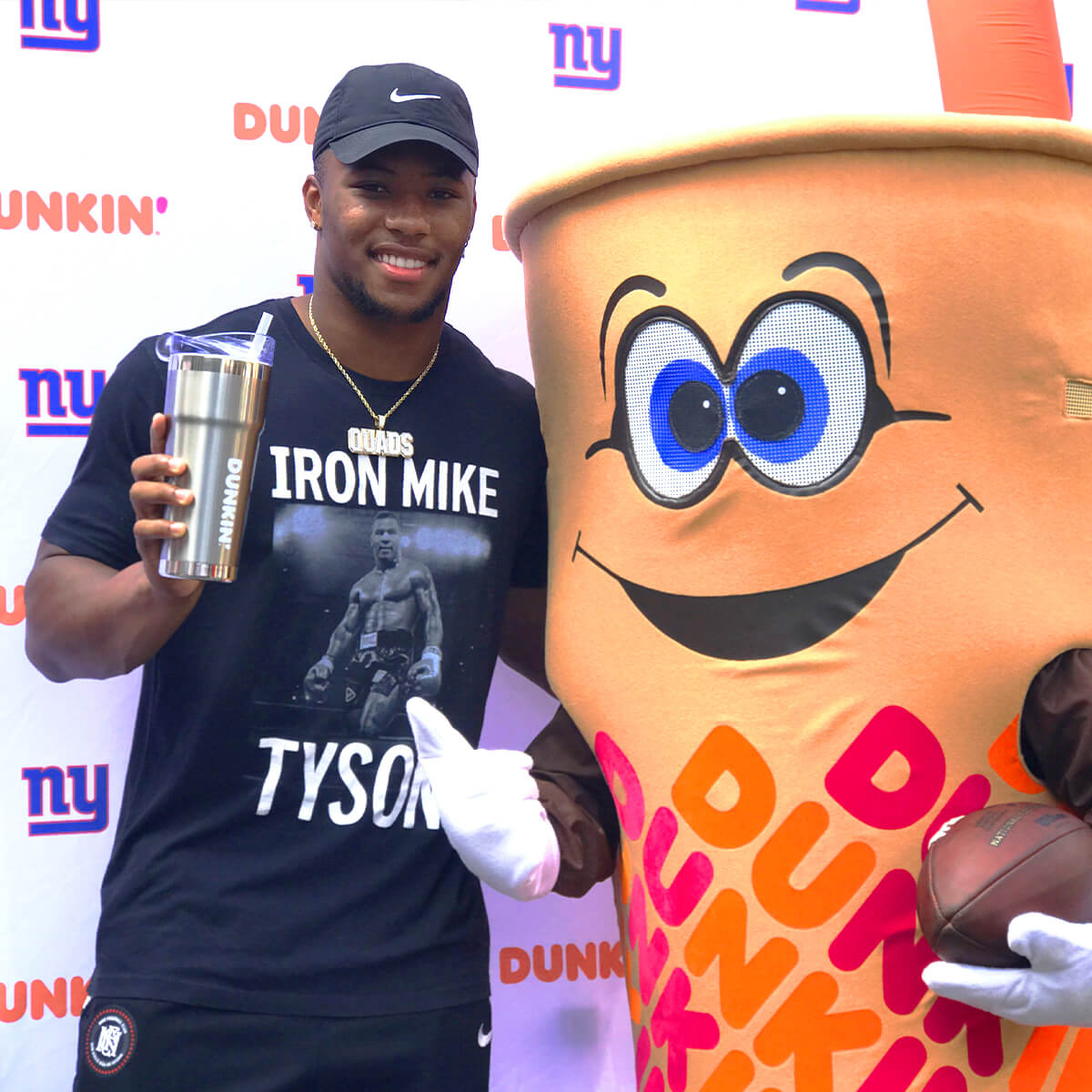 New York Giants Running Back, Saquon Barkley posing with the Dunkin' mascot and holding a Dunkin' branded cup