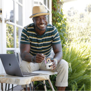 A man smiling outside near his laptop