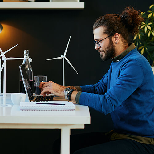 Man sitting at desk with a laptop, with miniature windmills.