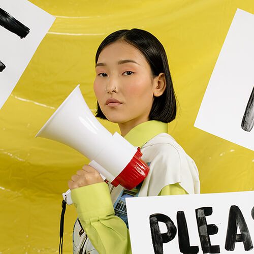 Asian woman with a megaphone surrounded by protest signs.