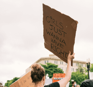 Picture of a person holding a protest sign saying "Girls Just Wannna Have Rights".
