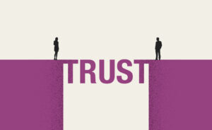 Two people stand facing each other on opposite sides of a bridge that spells trust