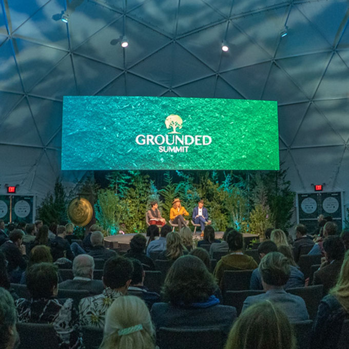 Three people speaking on stage at the Grounded Summit in front of an audience