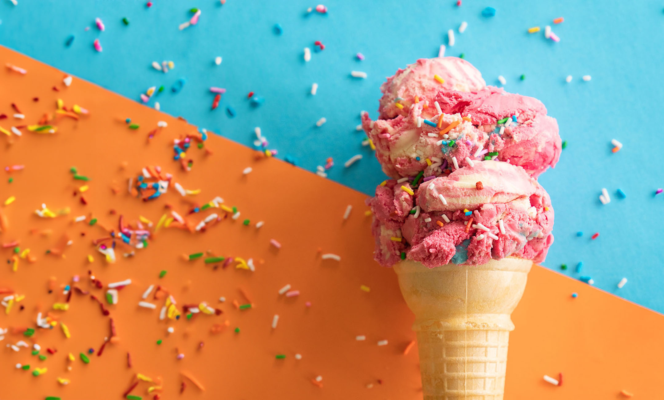 Pink and white swirled ice cream with multi-color sprinkles on a cone