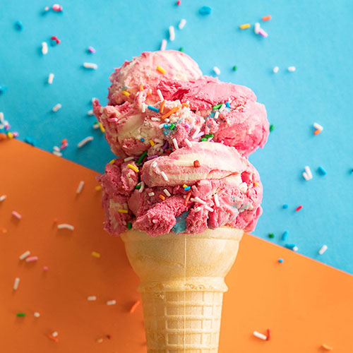 Pink and white swirled ice cream with multi-color sprinkles on a cone