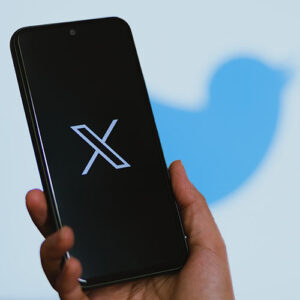 X logo on phone with Twitter bird logo in background