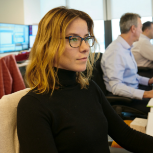 Woman wearing a black turtleneck and glasses sitting at a desk in an office