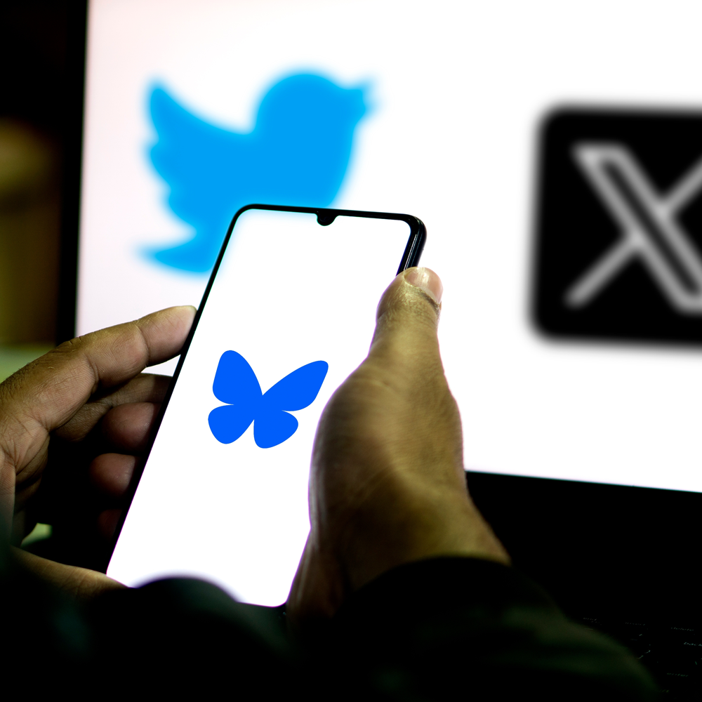 Person holding a phone with the blue sky logo displayed, and the twitter and x logos in the background.